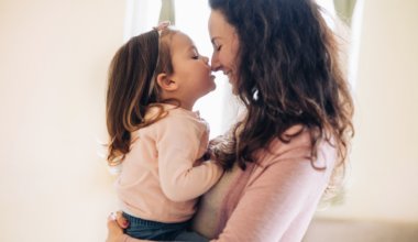 A mother kissing her daughter, depicting that she's embracing her unique motherhood journey with confidence.